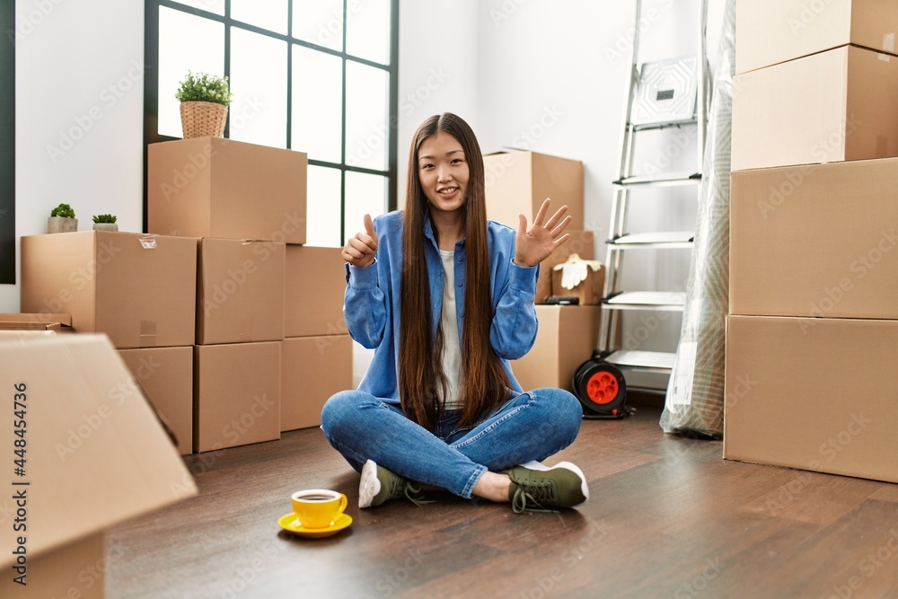 Canvas Prints Young chinese girl sitting on the floor at new home showing and pointing up with fingers number six while smiling confident and happy.