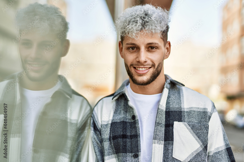 Wall mural Young hispanic man smiling happy standing at the city.