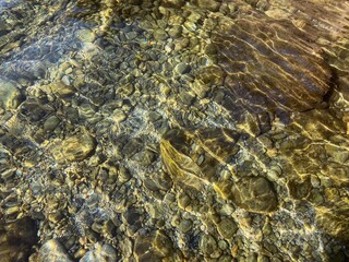 Pebbles stones gravel in sea water. Shiny transparent crystal clear water with sunlight on rippled waves. Zen, relax, summer. Colored pebbles on ocean floor.