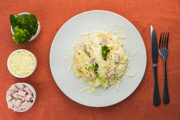 Delicious Fettuccine with white sauce, broccoli, turkey breast cubes and grated cheese. Selective focus. Top view.