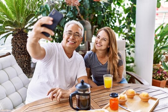 Middle age hispanic couple having breakfast making selfie by the smartphone at the terrace.