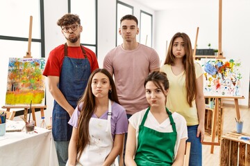 Group of five hispanic artists at art studio puffing cheeks with funny face. mouth inflated with...