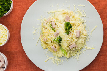 Delicious Fettuccine with white sauce, broccoli, turkey breast cubes and grated cheese. Selective focus. Top view.