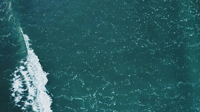 Top down view of wave rolling from left to right. White foamy pattern on water surface. Natural abstract background.