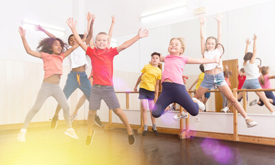 Group of happy sporty kids with female teacher training in modern dance studio, jumping together