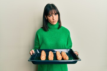 Young hispanic woman holding homemade bread skeptic and nervous, frowning upset because of problem....