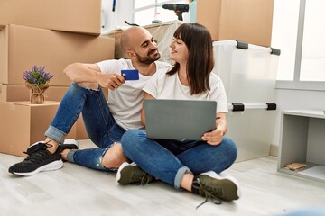 Young hispanic couple smiling happy using laptop and credit card at new home.