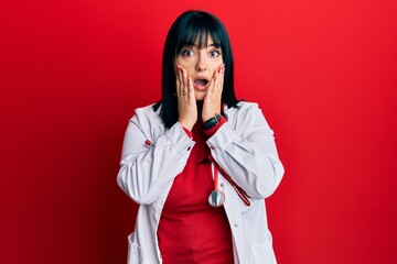 Young hispanic woman wearing doctor uniform and stethoscope afraid and shocked, surprise and amazed...