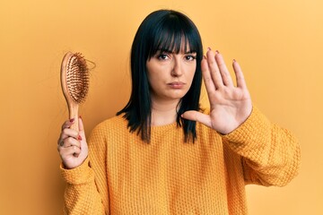 Young hispanic woman holding comb loosing hair with open hand doing stop sign with serious and...