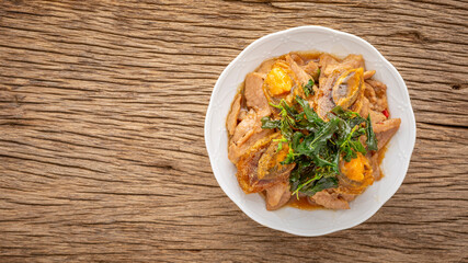 Pad Ka Prao Kai Yeow Ma, Thai food, basil stir fried century egg and sliced pork with crispy basil leaves on top in ceramic plate on rustic natural wood texture background with copy space, top view