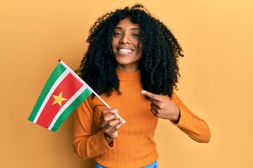 African american woman with afro hair holding suriname flag smiling happy pointing with hand and finger