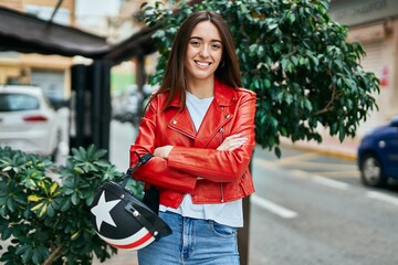 Young hispanic woman smiling happy holding moto helmet at the city.