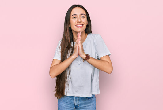 Young hispanic girl wearing casual white t shirt praying with hands together asking for forgiveness smiling confident.
