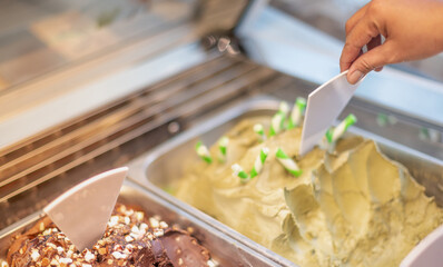 Female hand of a saleswoman in an ice cream parlor takes a scoop of ice cream in the store.