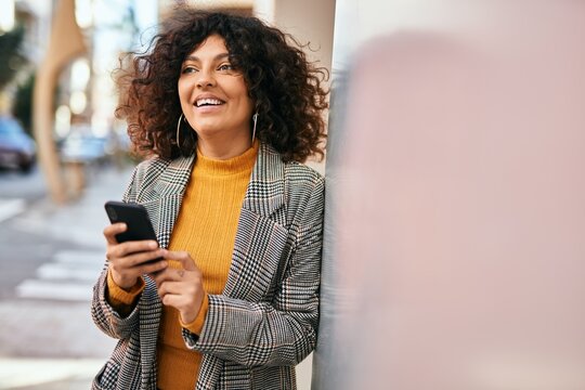 Young hispanic businesswoman smiling happy using smartphone at the city.
