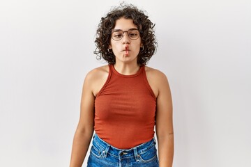 Young hispanic woman wearing glasses standing over isolated background making fish face with lips, crazy and comical gesture. funny expression.