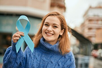 Young caucasian girl smiling happy holding blue awareness ribbon at the city.