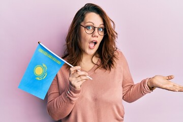 Young caucasian woman holding kazakhstan flag celebrating achievement with happy smile and winner expression with raised hand