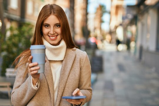 Young redhead girl using smartphone drinking coffee at the city.