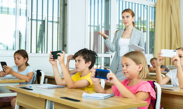 Portrait of preteen pupils using mobile phones during lesson in elementary school
