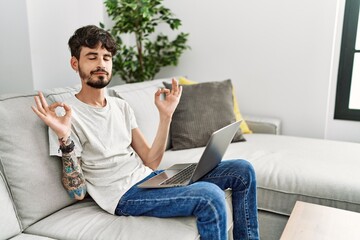 Hispanic man with beard sitting on the sofa relax and smiling with eyes closed doing meditation gesture with fingers. yoga concept.