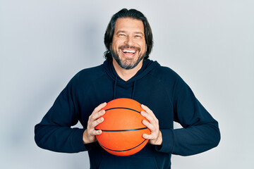Middle age caucasian man holding basketball ball smiling and laughing hard out loud because funny crazy joke.