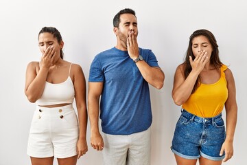 Group of young hispanic people standing over isolated background bored yawning tired covering mouth with hand. restless and sleepiness. - obrazy, fototapety, plakaty