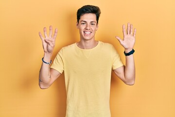 Young hispanic man wearing casual yellow t shirt showing and pointing up with fingers number nine...