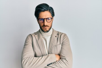 Young hispanic man wearing business jacket and glasses skeptic and nervous, disapproving expression on face with crossed arms. negative person.