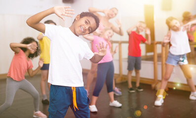 Portrait of cheerful african boy dancing with other children during group class in dance studio..