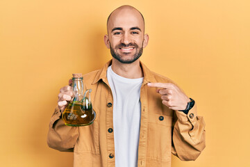 Young bald man holding olive oil can smiling happy pointing with hand and finger