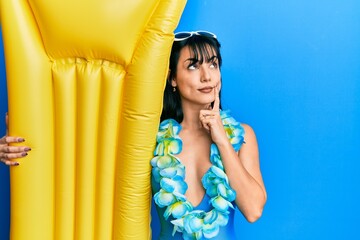 Young brunette woman with bangs wearing swimsuit and holding summer float serious face thinking...