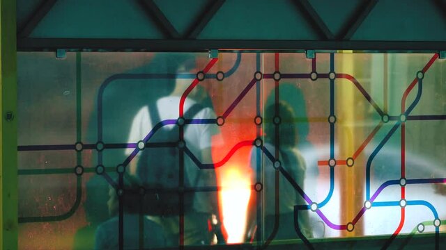 People stand at the bus stop waiting for public transport to arrive. Pouring rain. Unrecognizable commuters silhouettes. Trolleybus and shuttle bus stop with transparent glass and color applique.