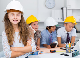Girl in color helmet builder with collective architects near notebook