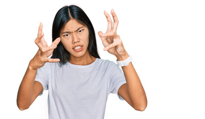 Beautiful young asian woman wearing casual white t shirt shouting frustrated with rage, hands trying to strangle, yelling mad