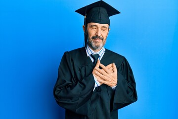 Middle age hispanic man wearing graduation cap and ceremony robe smiling with hands on chest with closed eyes and grateful gesture on face. health concept.