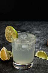Pisco glass. White drink in glass tumbler with ice and lemon on black marble background.