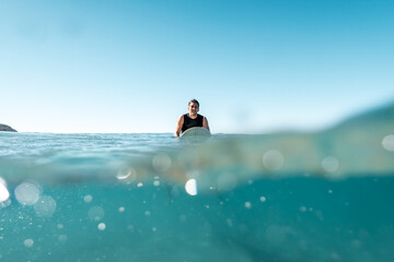 Surfer Sitting on His Board Looking to the Camera in a Sunny Day. Split Shot.Water Sport Concept