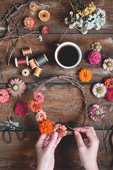 Overhead shot of female hands making a flower wreath on a rustic wooden table