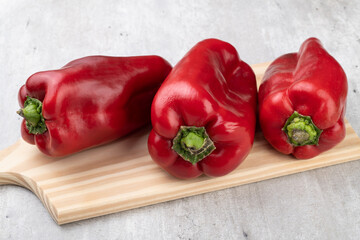 Three red bell peppers over wooden board