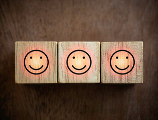 Close-up three smiling face icons with success light on wooden blocks on wood background. Business service rating concept.