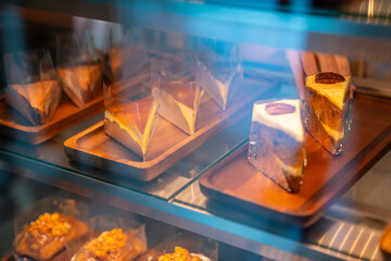 Asian woman coffee shop employee placing pastry and cake in bakery refrigerator showcase at cafe. Female waitress preparing restaurant for service to customer. Small business and part time job concept