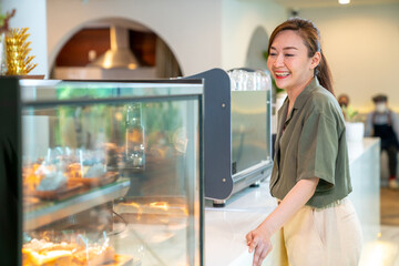 Fototapeta na wymiar Asian woman coffee shop employee barista working at cafe. Smiling female waitress cashier taking order coffee and bakery from customer. Small business owner and part time job working concept