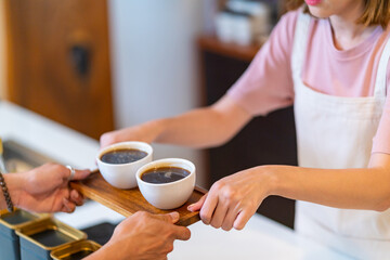 Asian woman coffee shop waitress barista serving hot coffee to customer on bar counter at cafe. Female restaurant cashier taking order from client. Small business owner and part time working concept