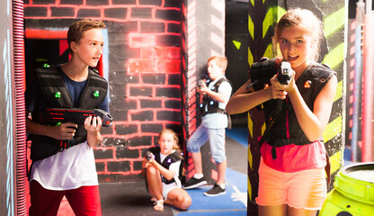 Fototapeta na wymiar Excited teen kids aiming laser guns at other players during lasertag game in dark room..