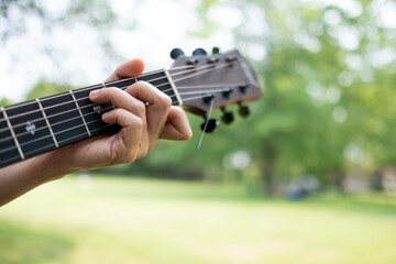 guitar chord played outdoors in a green park with trees as background
