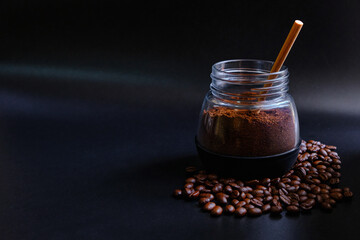 Fresh aromatic ground coffee in a glass jar with a wooden spoon on black background. There are heaps of coffee beans.
