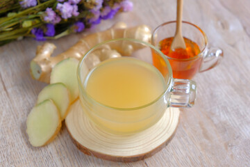 Obraz na płótnie Canvas glass cup of hot ginger tea with ginger root (rhizome) slices and honey on wooden background. Herbal medicine plant and supplement concept.