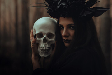 frightening evil witch in black rags holds a dead man's skull in her hands for a dark ritual