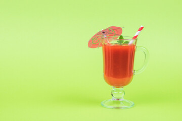 A glass glass on a leg with an umbrella and a cocktail tube on a green background.